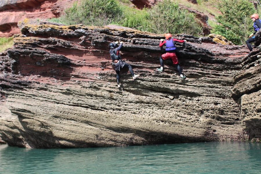 Torquay: Coasteering 5</em> Geopark Tour in Torquay – Maidencombe Geopark coast: what makes this stretch of water special’ /><br />
Torquay’s shoreline can look pretty much like any rocky coast until you do something on it. Coasteering changes your view fast, because suddenly you are moving through the intertidal zone, where land and sea constantly trade places. The Maidencombe area is known for striking coastal formations, and that is the point here: you are not just testing your nerve, you are learning how the coast works.</p>
<p><p>This tour is set in Devon’s UNESCO Geopark, so the guides bring the geology into the walk. You will hear stories about how the landscape is shaped, and it gives the trip more meaning than just jumps. It also makes the places you scramble past feel purposeful, like each cave mouth or rocky ledge has a reason it exists.</p>
</p>
<p><p>One more thing I appreciate is that the tour is built for different comfort levels. You still get the adventure, but you are not automatically shoved into the highest or most technical options if you are not ready.</p>
</p>
<div class="twil" style="margin: 20px 0; padding: 15px 0;"><p>More coasteering in Devon:</p><ul style="margin: 10px 0; padding-left: 0; list-style: none;"><li style="margin: 0 0 12px 0; padding: 0 0 12px 0; border-bottom: 1px solid #eee; line-height: 1.4;"><a href="https://thebritishguide.com/newquay-coasteering/">Newquay: Coasteering</a><br><span style="font-size: 0.82em; color: #555;"><span style="color: #1D3557;">★</span> 4.9 &nbsp;&middot;&nbsp; 21 reviews</span></li><li style="margin: 0 0 12px 0; padding: 0 0 12px 0; border-bottom: 1px solid #eee; line-height: 1.4;"><a href="https://thebritishguide.com/pembrokeshire-coasteering-adventure-at-stackpole-quay/">Pembrokeshire: Coasteering Adventure at Stackpole Quay</a><br><span style="font-size: 0.82em; color: #555;"><span style="color: #1D3557;">★</span> 5.0 &nbsp;&middot;&nbsp; 6 reviews</span></li><li style="margin: 0; padding: 0; border-bottom: none; line-height: 1.4;"><a href="https://thebritishguide.com/cornwall-coasteering-cliff-jumping-adventure/">Cornwall: Coasteering & Cliff Jumping Adventure</a><br><span style="font-size: 0.82em; color: #555;"><span style="color: #1D3557;">★</span> 5.0 &nbsp;&middot;&nbsp; 5 reviews</span></li></ul></div><h2 id="meeting-at-the-thatched-tavern-and-getting-kitted-up">Meeting at The Thatched Tavern and getting kitted up</h2>
<p> Geopark Tour in Torquay – Meeting at The Thatched Tavern and getting kitted up’ /><br />
You meet outside <strong>The Thatched Tavern</strong> and look for the orange van. It is a straightforward setup, and that matters because coasteering is time-sensitive. The whole activity depends on being geared up and moving while conditions are right.</p>
<p><p>Once you arrive, you are kitted out with the gear that matters for safety and warmth: wetsuit, helmet, buoyancy aid, gloves, and old shorts. There is also secure storage for belongings, which is a real relief because you do not want to think about keys or phones while you are handling slippery rock.</p>
</p>
<p><p>Before you head out, you get a safety briefing. That briefing is not just legal talk. It sets you up to understand how the route is navigated, what types of scrambling to expect, and how jumping or entering the water should feel. You also get clear guidance on what you should and should not attempt.</p>
</p>
<p><p>Hot drinks are included too. It is a small detail, but after being in cold water and salt air, warmth helps you enjoy the rest of the experience instead of simply surviving it.</p>
</p>
<h2 id="safety-first-but-not-stiff-how-the-guides-set-your-pace">Safety first, but not stiff: how the guides set your pace</h2>
<p><img width="900" height="599" decoding="async" src=
